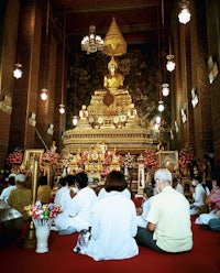 a group of people sitting in front of a golden buddha